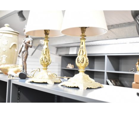 A pair of gilt metal table lamps with woollen shades, supported on a step base and decorated with floral patterns, (2).
