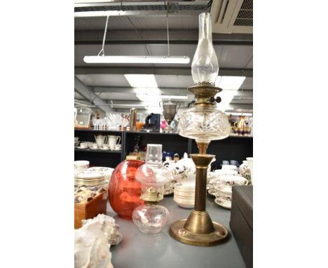 An early 20th century brass oil lamp with glass chimney and red shade, having arts and craft stylised base, H72cm, sold toget