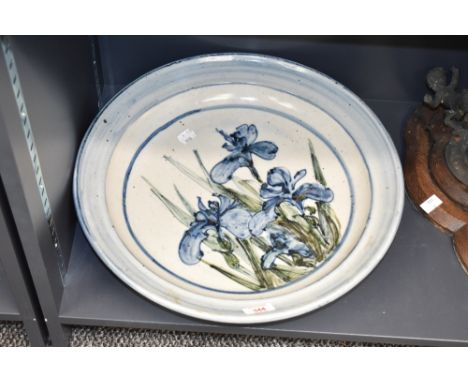 A large and decorative art pottery stoneware charger, decorated with iris flowers within blue borders, the reverse with paint