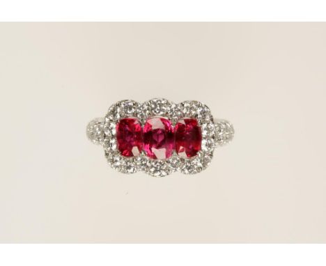 A THREE STONE RUBY AND DIAMOND DRESS RING, the three cushion-cut rubies c.2.04cts (total) with a border of brilliant-cut diam