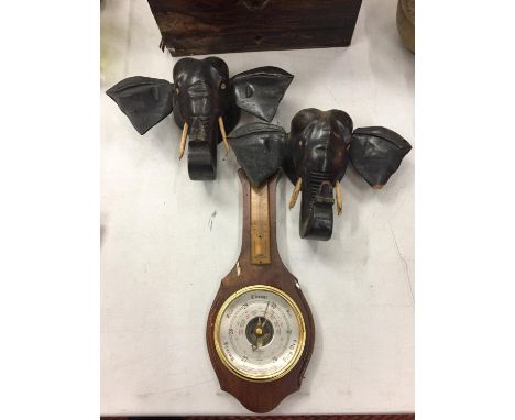 A WOODEN BOX, TWO WOODEN WALL MOUNTED ELEPHANT HEADS AND A BAROMETER 