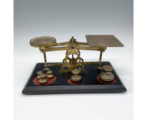 Brass scale mounted on black wooden base. Scale weights included are 1/2 oz. to 4 oz. Made in England impressed mark. Issued: