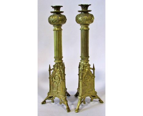 A pair of 19th century Puginesque brass candlesticks, with flared pomegranate shaped cradles, over fluted columns a d archite