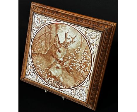 A decorative ceramic tile mounted in a wooden frame as a trivet, depicting a pair of roe deer in sepia tones together with an