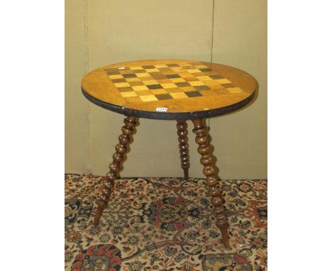 A 19th century chequerboard games table, in mixed woods, raised on three bobbin supports, 62cm diameter 