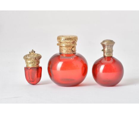 Two 19th century ruby glass spherical scent bottles and a ruby glass vinaigrette, the largest with a silver gilt engraved sta