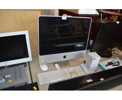 An Apple I-mac computer with keyboard, mouse, power cable, external speaker, Apple TV remote, and software install discs