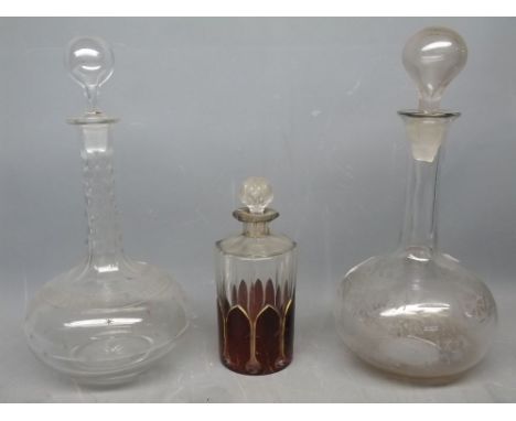 Two clear glass decanters, one with a facetted stem and stopper, the other with etched floral design, together with a further
