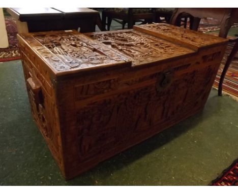 Oriental camphor wood heavily carved trunk with stepped top, with Oriental scenes carved throughout, side handles, decorative