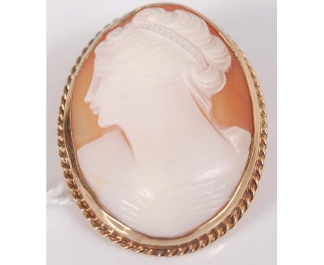 A 9ct yellow gold oval shell cameo brooch depicting a Roman woman, with ropetwist surround and roller-catch fastening, dimens