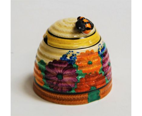 A Clarice Cliff preserve pot and cover, in the Gay Day pattern, the cover surmounted by a bee (loss to wing) having printed C