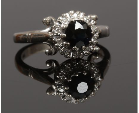 An 18ct white gold ring floriform set with a faceted black stone and diamonds, bordered by scrolling shoulders.
