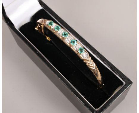 A cased 9ct gold bangle set with five emeralds interspersed with diamonds, gross weight 11.3 grams.