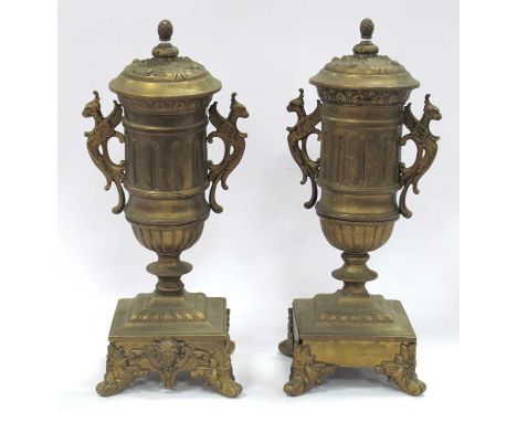 A pair of gilded brass vases with finial tops, twin handles as grotesque birds, on scroll feet, 30cm h.