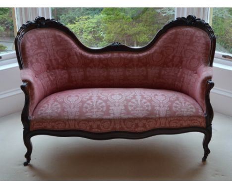 A Victorian rosewood double chair back sofa, the scroll and foliate carved top rail above a button down upholstered back, arm