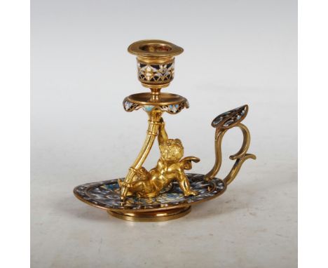 A late 19th/ early 20th century gilt metal and champleve enamel chamber candlestick, the oval base set with a putti supportin