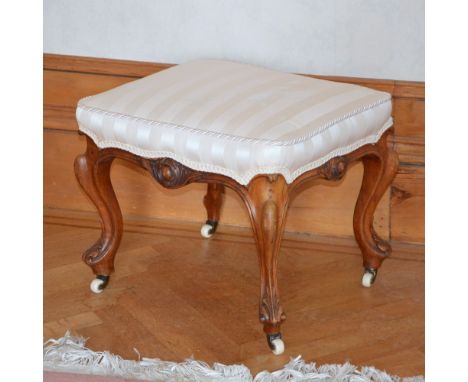 A Victorian mahogany stool, the striped upholstered rectangular top raised on foliate carved cabriole supports and white cera