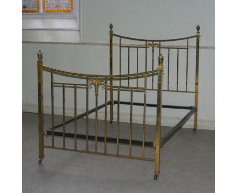 A late Victorian brass double bed, the head and footboard with concave top rails above vertical bars centred with a scrolling