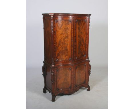 A George III style mahogany serpentine cupboard, the moulded cornice and dentil frieze above a pair of cupboard doors opening