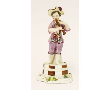 A Meissen figure of a young boy,c.1745, playing a pipe, decorated in coloured enamels, standing on an upturned coopered milk 