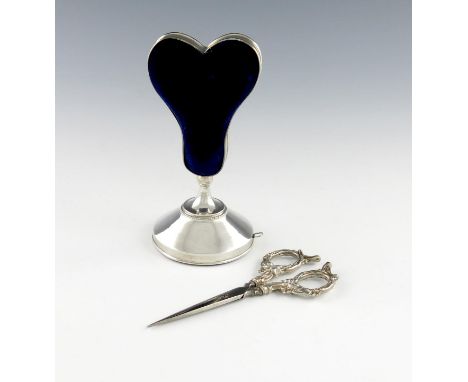 An Edwardian silver pin cushion, scissor stand and tape measure, by Arthur Pennington, Birmingham 1908, shaped heart form, on