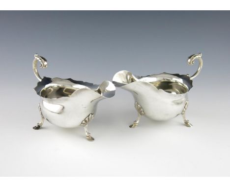 A pair of silver sauce boats, by Walker and Hall, Sheffield 1924, oval form, wavy-edge border, leaf capped scroll handles, on