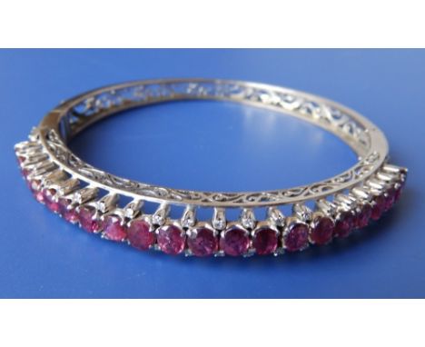 A palladium coloured bangle set with 21 oval cut rubies within two rows of small diamonds.