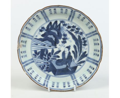 A Japanese dish with lotus petal rim edged in brown enamel. Painted in underglaze blue with a seated figure under a panelled 