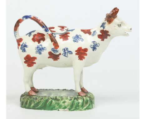 A 19th century creamware cow creamer. Formed as a short horned dairy cow raised on a naturalistic plinth and with coloured en