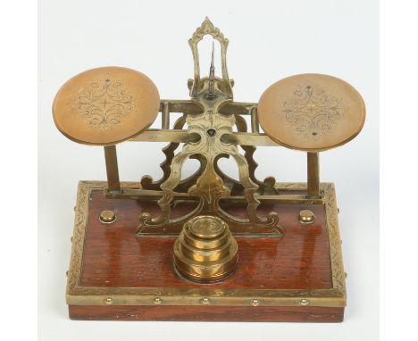 A set of Victorian brass postal scales and four graduated weights. With engraved decoration and raised on an oak plinth, 17.5