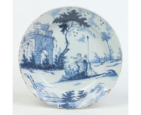 A London Delft blue and white charger. Painted with a landscape incorporating a folly, sponged trees and a courting couple. S