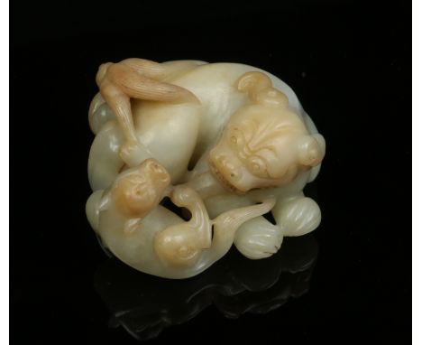 An antique Chinese celadon jade carving of a lion dog and its young with russet markings. The female beast modelled recumbent