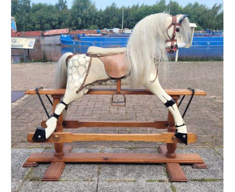 A wooden rocking horse, dapple grey with silver mane, a Save the Children ribbon pinned to the reins, on a trestle rocker fra