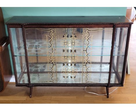 A 1950s display cabinet, the shaped rectangular top having cockbeaded edge over two sliding glass doors, opening to mirror ba