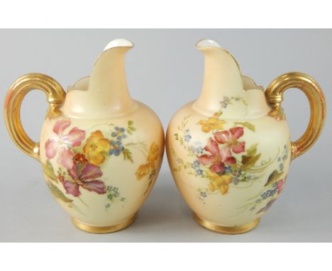 A pair of Royal Worcester porcelain ewers, each painted with flowers on a blush ivory ground, picked out in gilt, printed mar