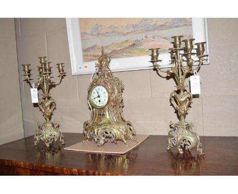 A cast brass reproduction clock garniture, the rococo style mantel clock fitted white enamel arabic dial, flanked by a pair o