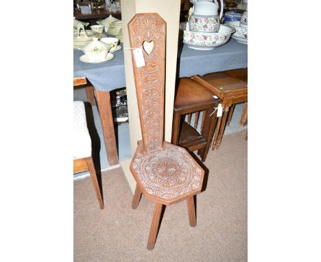 A carved oak spinning stool, with heart-shaped cut-out to back and decorative motifs carved overall, diamond chequered taperi