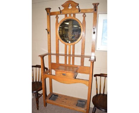 An Art Nouveau design oak hall stand, the pierced cornice above circular bevelled mirror panel, glove drawer below and undert