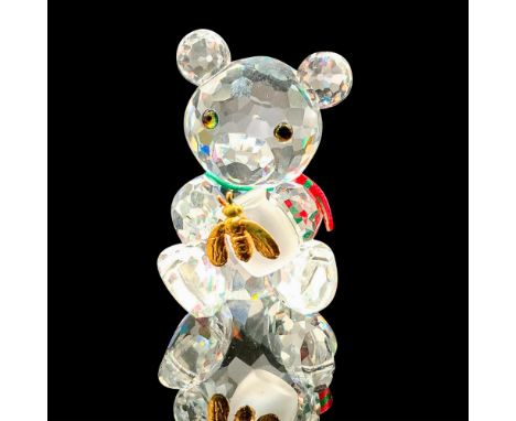 A clear crystal figure of a bear sitting down on their bottom while holding a honey pot that is decorated with a gold-colored