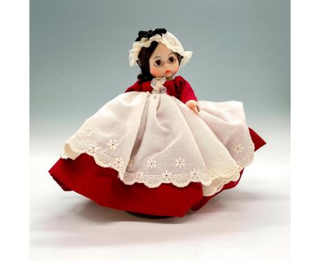 Doll wears a burgundy dress and a white bonnet and apron. This item has a base included. This item has its original box. Box 