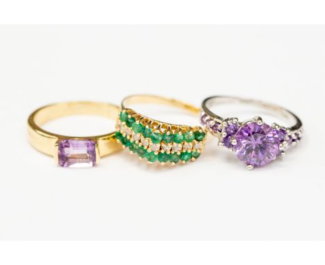 3 x 14 k marked dress rings, 1 white gold with purple stones and two yellow gold, 1 emerald cut amethyst, 1 emerald and diamo