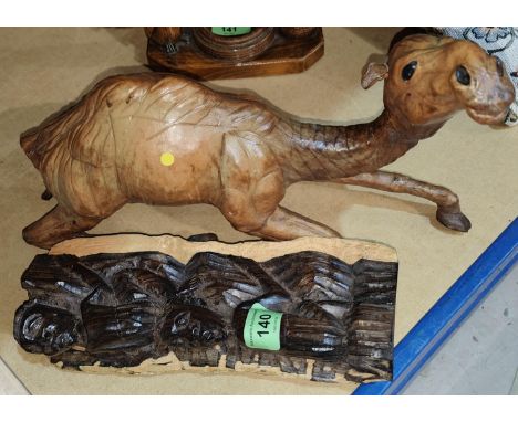 A leather model of a reclining camel with glass eyes length 39cm and a hardwood carving of a tribal group, ht. 24cm 