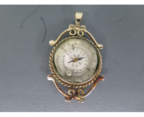 A yellow metal fob with compass to centre