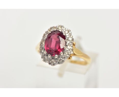 A YELLOW METAL GARNET AND DIAMOND CLUSTER RING, slightly raised cluster designed with a central claw set oval cut garnet, wit