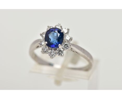 A SAPPHIRE AND DIAMOND CLUSTER RING, centring on a four claw set, oval cut blue sapphire, within a surround of round brillian