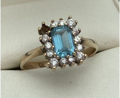 A 9ct gold blue topaz and clear stone dress ring. A square cut central blue topaz surrounded by small round cut clear stones 