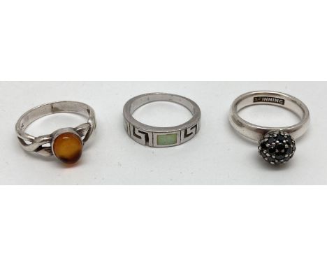 3 silver and white metal dress rings. A band style with Greek key detail set with opalite panels; an amber cabochon set ring 