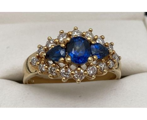 An 18ct gold, sapphire and diamond cluster style dress ring. Central oval cut sapphire with a teardrop cut sapphire to each s