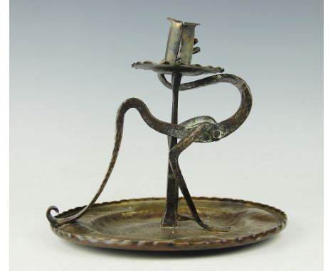 A German Arts and Crafts brass chamber stick, designed as a bird with long neck and tail with planished detailing and on circ