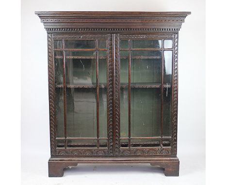 A Victorian carved oak bookcase, the glazed cupboard doors enclosing three internal shelves, carved with a decorative foliate